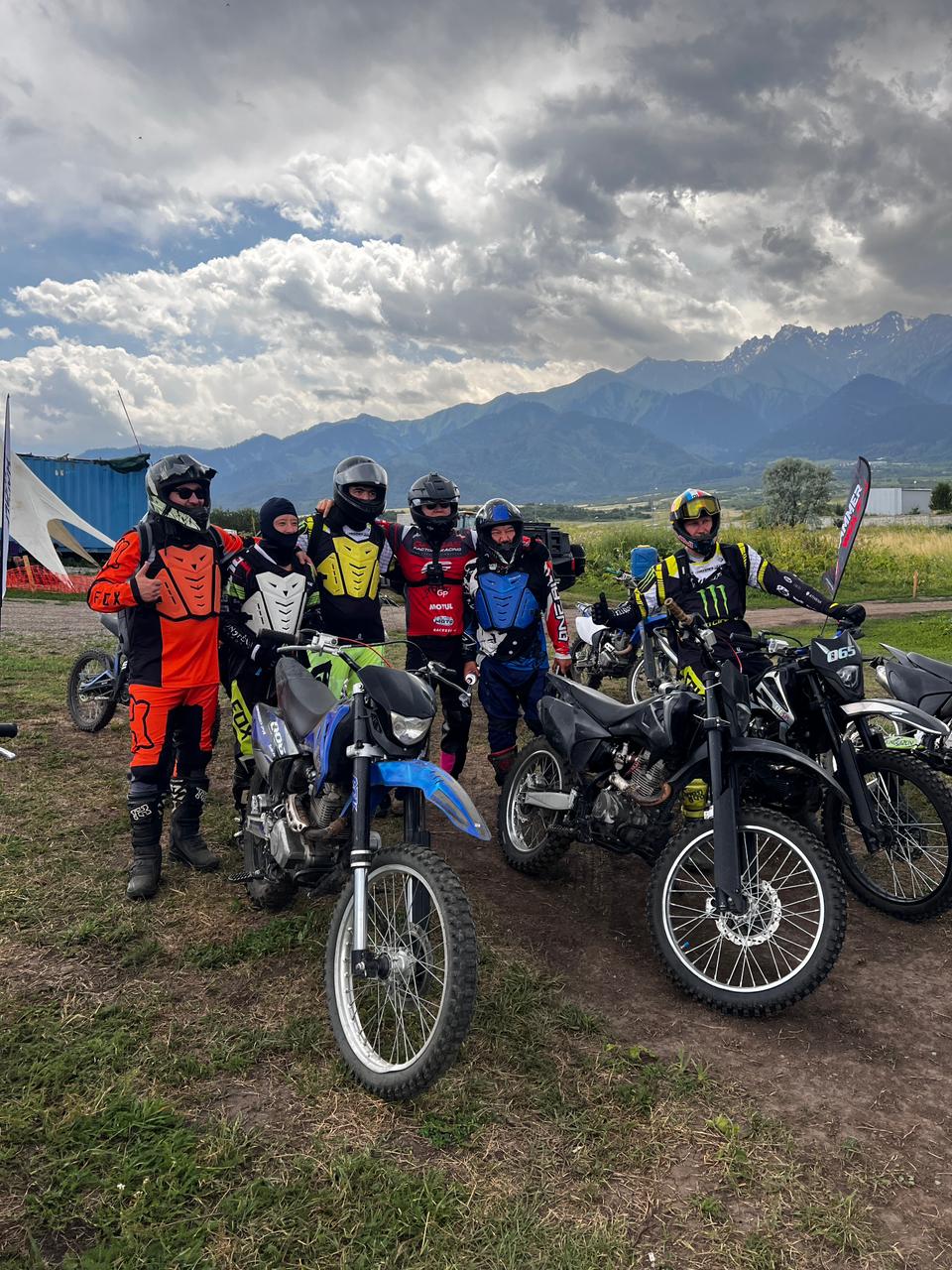 Группа райдеров Ex_travel с эндуро-байками на фоне облачных гор